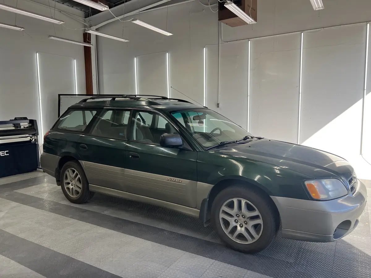 Green Subaru Outback before window tinting, factory glass (view 1)