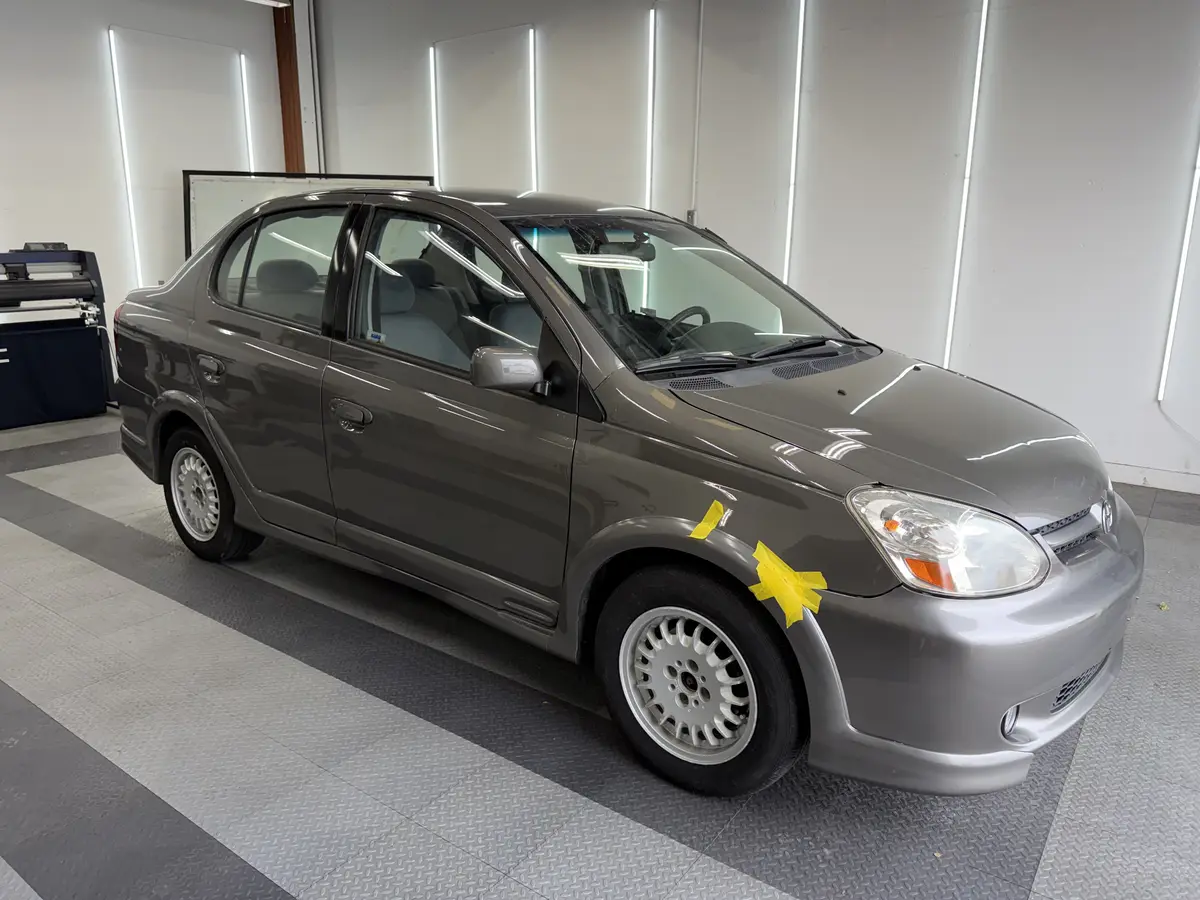 Gray Toyota Echo before window tinting, factory glass (view 1)
